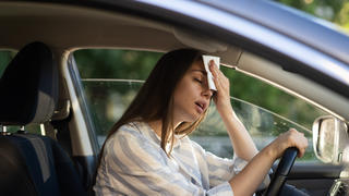 Eine Frau im Auto die sich an den Kopf fast, weil es zu heiß ist.