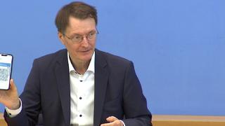 Während einer Pressekonferenz hält Karl Lauterbach sein digitales Impfzertifikat in die Kamera.