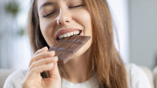 Frau beißt von Tafel dunkler Schokolade ab.