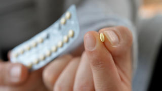 Frau hält Antibabypille zwischen zwei Fingern