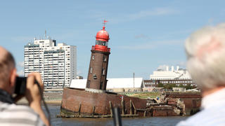 20.08.2022, Bremen, Bremerhaven: Schaulustige beobachten den abgesackten Moleturm in Bremerhaven. In der Nacht zum Donnerstag hatte sich die Nordmole, an deren Spitze das Leuchtfeuer mit dem roten Haupt steht, abgesenkt, wobei der rund 20 Meter hohe Turm in eine bedrohliche Schieflage geriet. Foto: Markus Hibbeler/dpa +++ dpa-Bildfunk +++