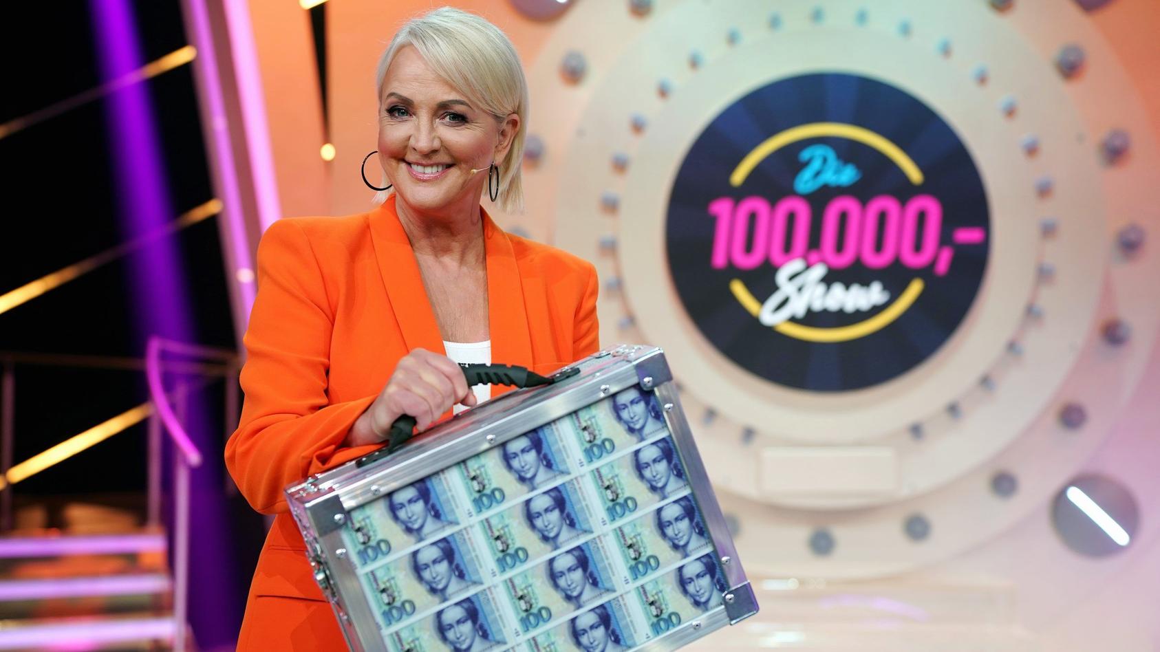 Ulla Kock am Brink hält Geldkoffer vor dem Logo der "100.000 Mark Show"