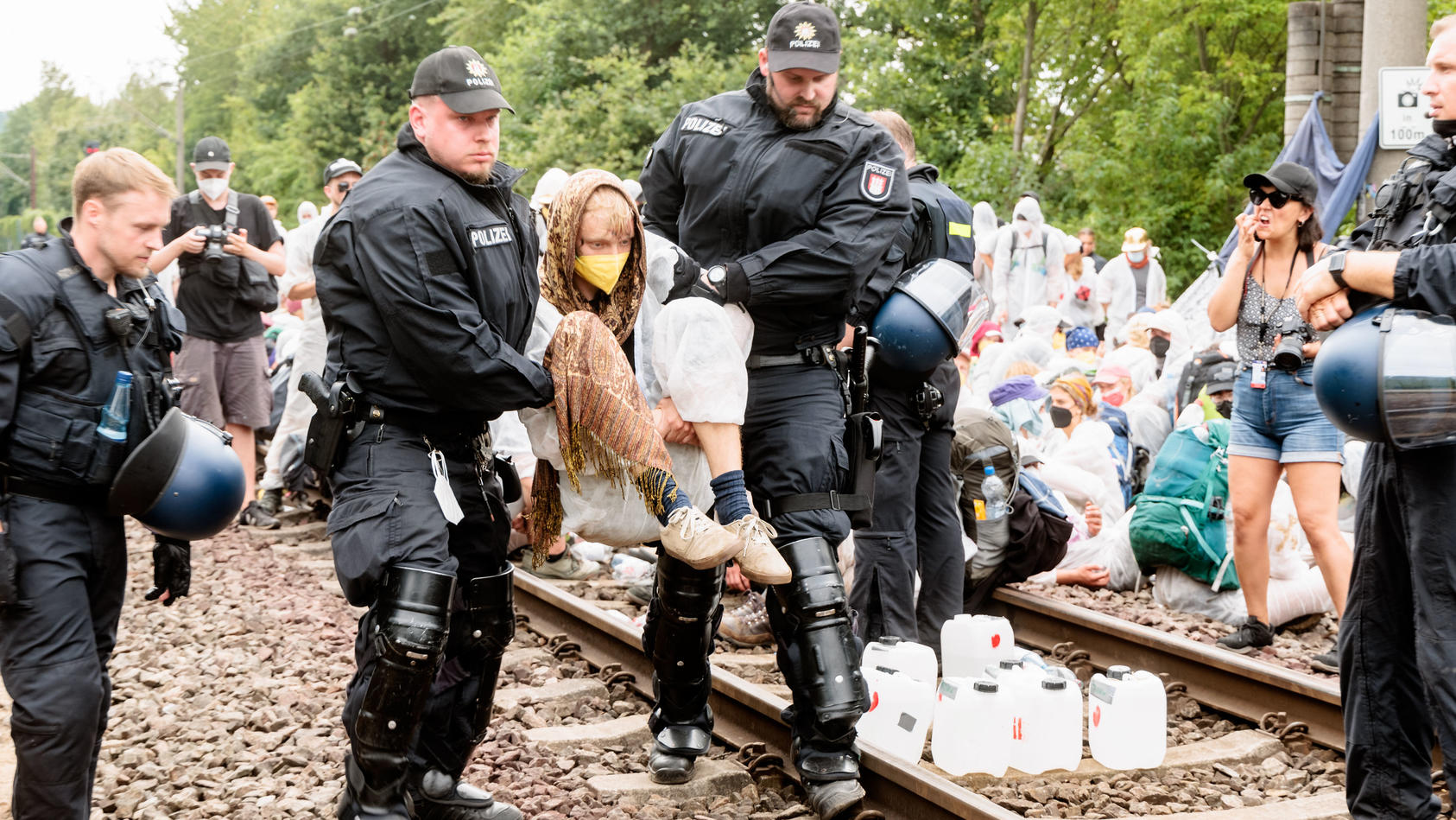 13.08.2022, Hamburg: Klima-Aktivisten die aus Protest Gleise im Hamburger Hafen besetzt haben, werden einzeln von Polizeibeamten von den Gleisen getragen. Klimaaktivisten haben in Hamburg an verschiedenen Stellen Blockaden initiiert, um für mehr Klim