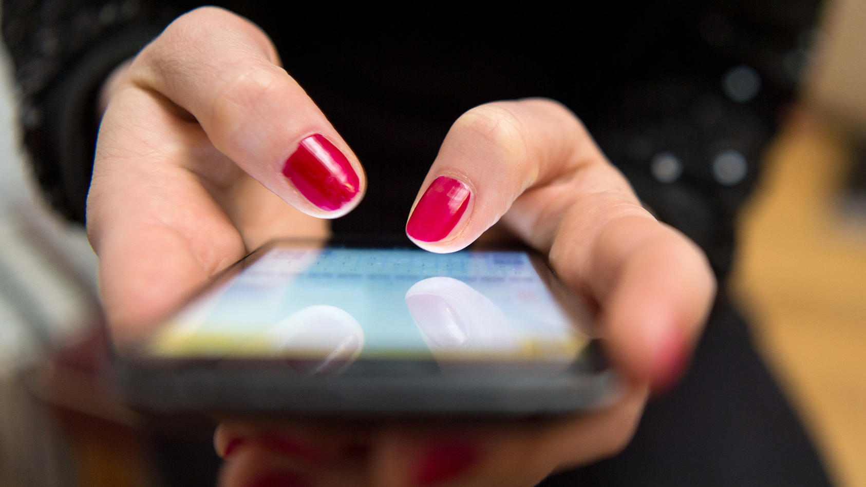 Person mit lackierten Fingernägeln hält Smartphone in den Händen und tippt. 