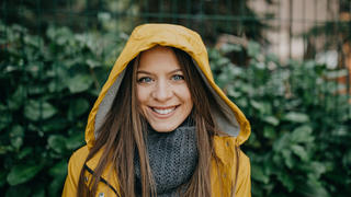 Ein Portrait einer Frau die eine gelbe Regenjacke trägt und lächelt.