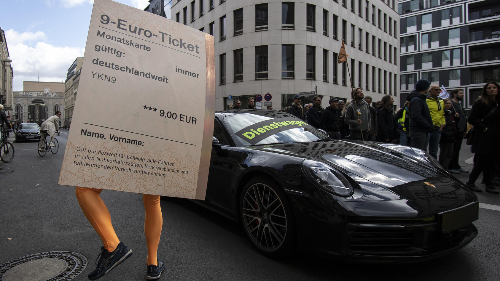 18.09.2022, Berlin: «Dienstwagen» steht auf einem Porsche 911 während ein Demonstrant mit einem übergroßen «9-Euro-Ticket» bei einer Protestaktion der Umweltschutz-Organisation Greenpeace vor der FDP-Bundeszentrale daneben steht. Nach Informationen v