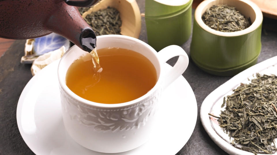 Grüner Tee wird aus einer Kanne in eine Teetasse gegossen.