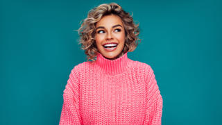 Frau in einem pinken Pullover steht vor einem blauen Hintergrund.