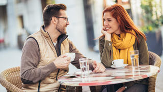 Junges Paar sitzt im Herbst vor einem Café und lächelt sich an