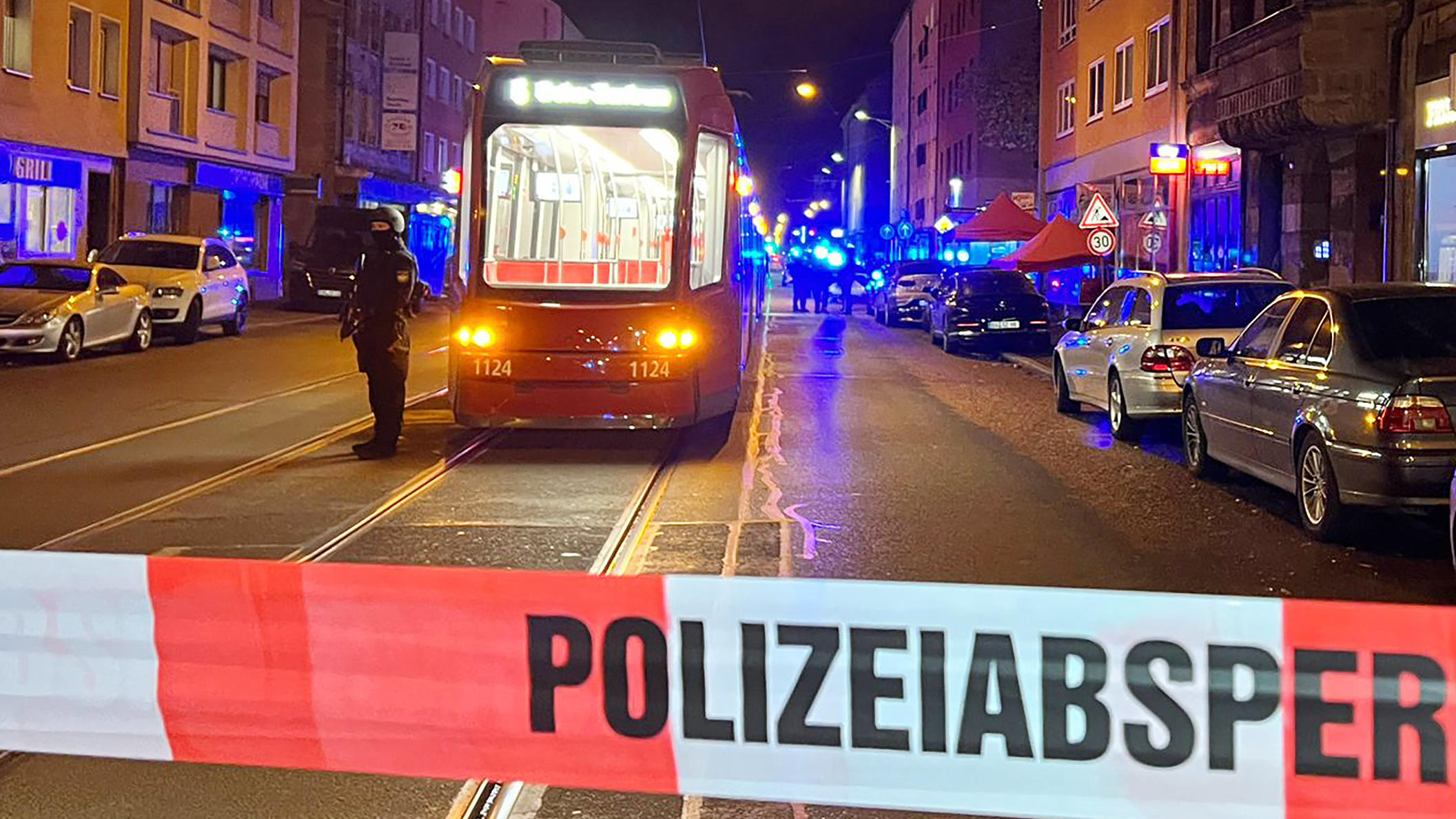 24.10.2022, Bayern, Nürnberg: Ein Polizist steht mit einer Maschinenpistole neben einer Straßenbahn hinter einer Polizeiabsperrung. Bei Schüssen in der Nürnberger Südstadt sind am Montagabend zwei Menschen schwer verletzt worden. Gegen 20.00 Uhr habe