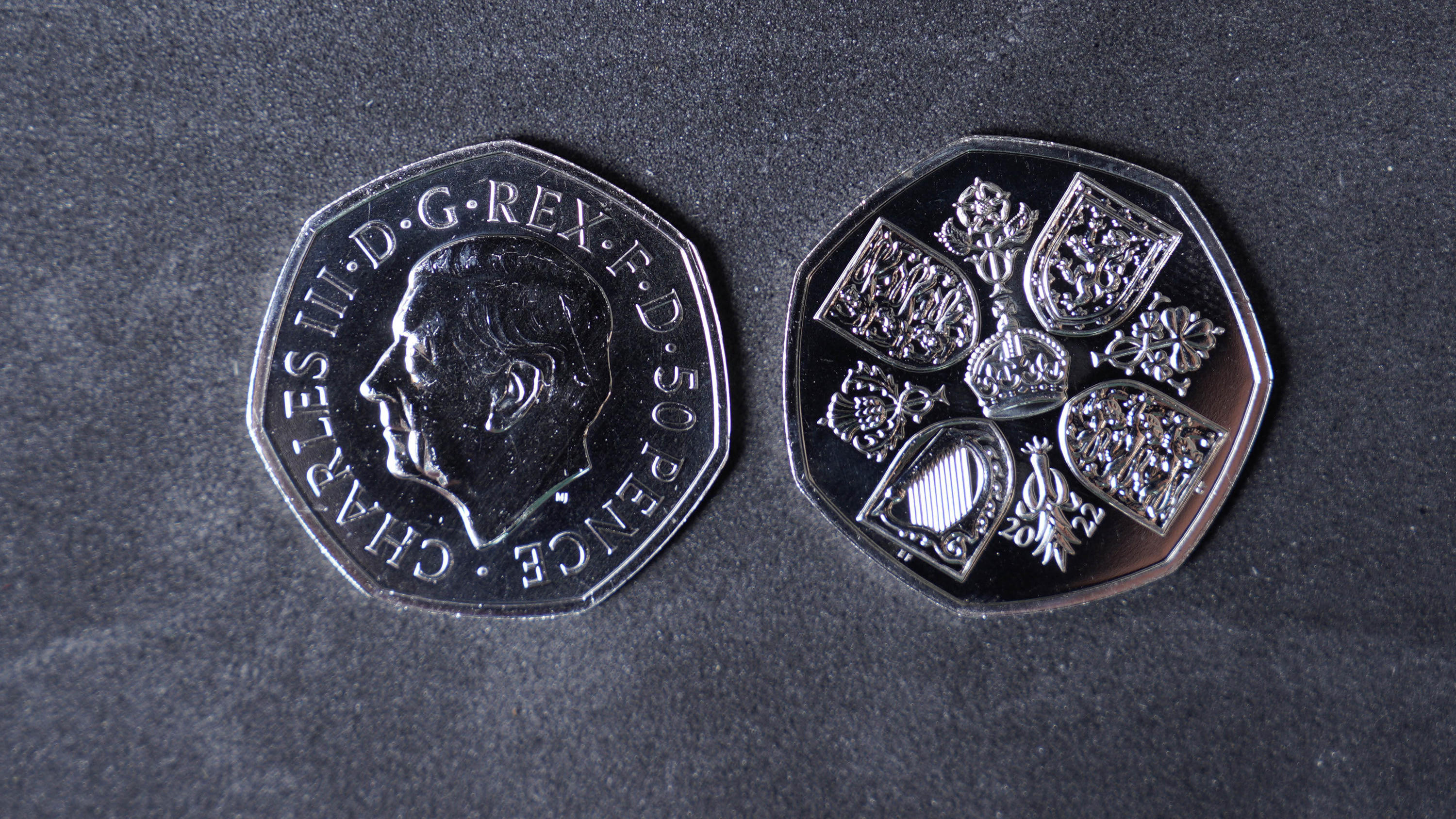 28.10.2022, Großbritannien, Pontyclun: Eine Geldmünze mit dem Konterfei des britischen König Charles III. (l) liegt neben einer Geldmünze, auf der die Rückseite abgebildet ist. Die ersten britischen Geldmünzen mit dem Konterfei des neuen Königs Charl