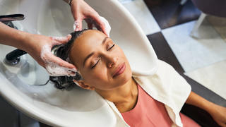 Eine Frau lässt sich beim Friseur am Waschbecken die Haare waschen.