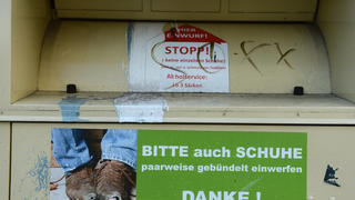 ARCHIV - Ein Kleidercontainer wirbt am 30.11.2012 in Berlin mit einem Foto von abgetragenen Schuhen um den Einwurf von Schuhen. Foto: Jens Kalaene/dpa (zu dpa: "Falsche Wohltäter im Konkurrenzkampf um Altkleider") +++(c) dpa - Bildfunk+++