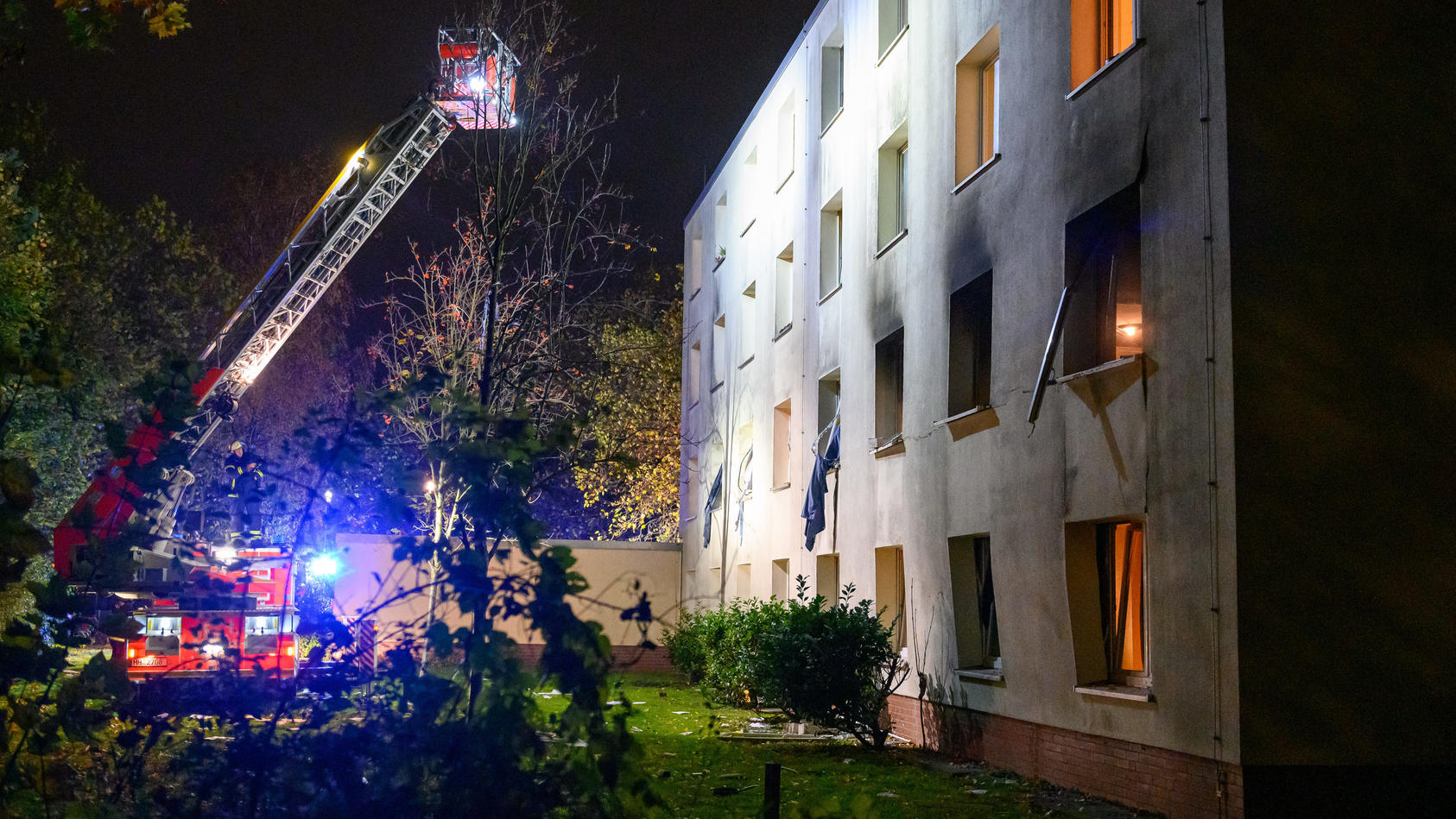 10.11.2022, Hamburg: Eine Drehleiter der Feuerwehr beleuchtet die verrußte und beschädigte Fassade des Gebäudes. Bei einer Explosion in einem Männerwohnheim für Bedürftige in Hamburg-Stellingen ist ein Mann am Donnerstagabend lebensgefährlich verletz