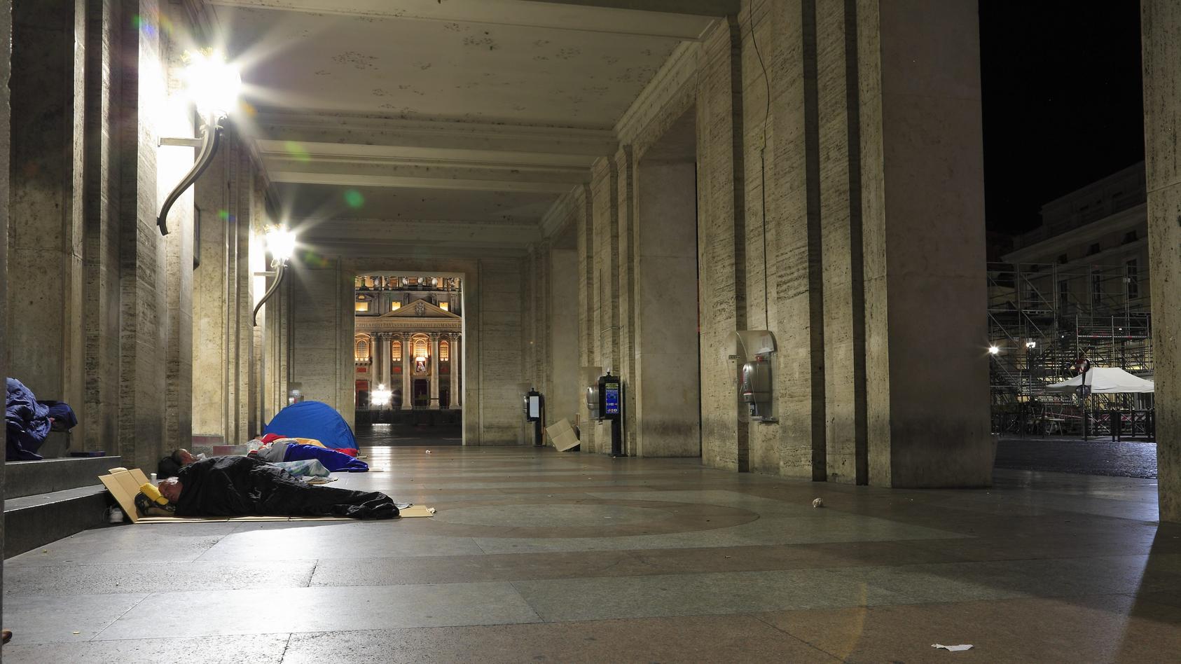 Obdachlose schlafen in der Vorhalle der Opera Romana Pellegrinaggi unweit des Petersplatzes. Im Bildhintergrund sind ein Teil des Petersplatzes sowie ein Teil des Petersdomes zu sehen. Ueber dem Hauptportal des Petersdomes ist noch das Bild von Mutte