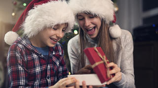 Junge und Mädchen öffnen gemeinsam ein Geschenk und freuen sich.