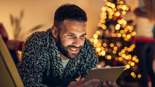 Samsung-Tablet: Ein Mann sitzt vor einem leuchtendem Weihnachtsbaum und ist lächelnd am Tablet.