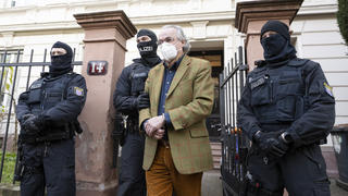 dpatopbilder - 07.12.2022, Hessen, Frankfurt/Main: Bei einer Razzia gegen sogenannte «Reichsbürger» führen vermummte Polizisten, nach der Durchsuchung eines Hauses Heinrich XIII Prinz Reuß (2.v.r.) zu einem Polizeifahrzeug. Die Bundesanwaltschaft hat am Mittwochmorgen mehrere Menschen aus der sogenannten Reichsbürgerszene im Zuge einer Razzia festnehmen lassen. Zahlreiche Beamte seien in mehreren Bundesländern im Einsatz, sagte eine Sprecherin der Karlsruher Behörde . Foto: Boris Roessler/dpa +++ dpa-Bildfunk +++