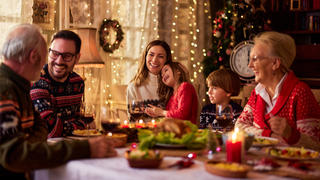 Familie sitzt am Weihnachtstisch und lacht.