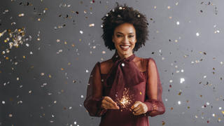 Eine lächelnde, afroamerikanische Frau in einem roten Kleid und Wunderkerzen in der Hand.