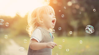 Little blonde boy playing with soap bubbles in a park.
