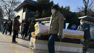 31.12.2022, China, Beijing: Arbeiter schieben einen Sarg vor ein Krematorium. China hat Anfang dieses Monats viele seiner strengen Corona-Beschränkungen aufgehoben, so dass sich das Virus rasch ausbreiten konnte. Die Zahl der Einäscherungen ist um ein Vielfaches gestiegen. Viele Bestattungsinstitute sind ausgelastet und bitten die Familien die Beerdigungen zu verschieben. Foto: Ng Han Guan/AP/dpa +++ dpa-Bildfunk +++