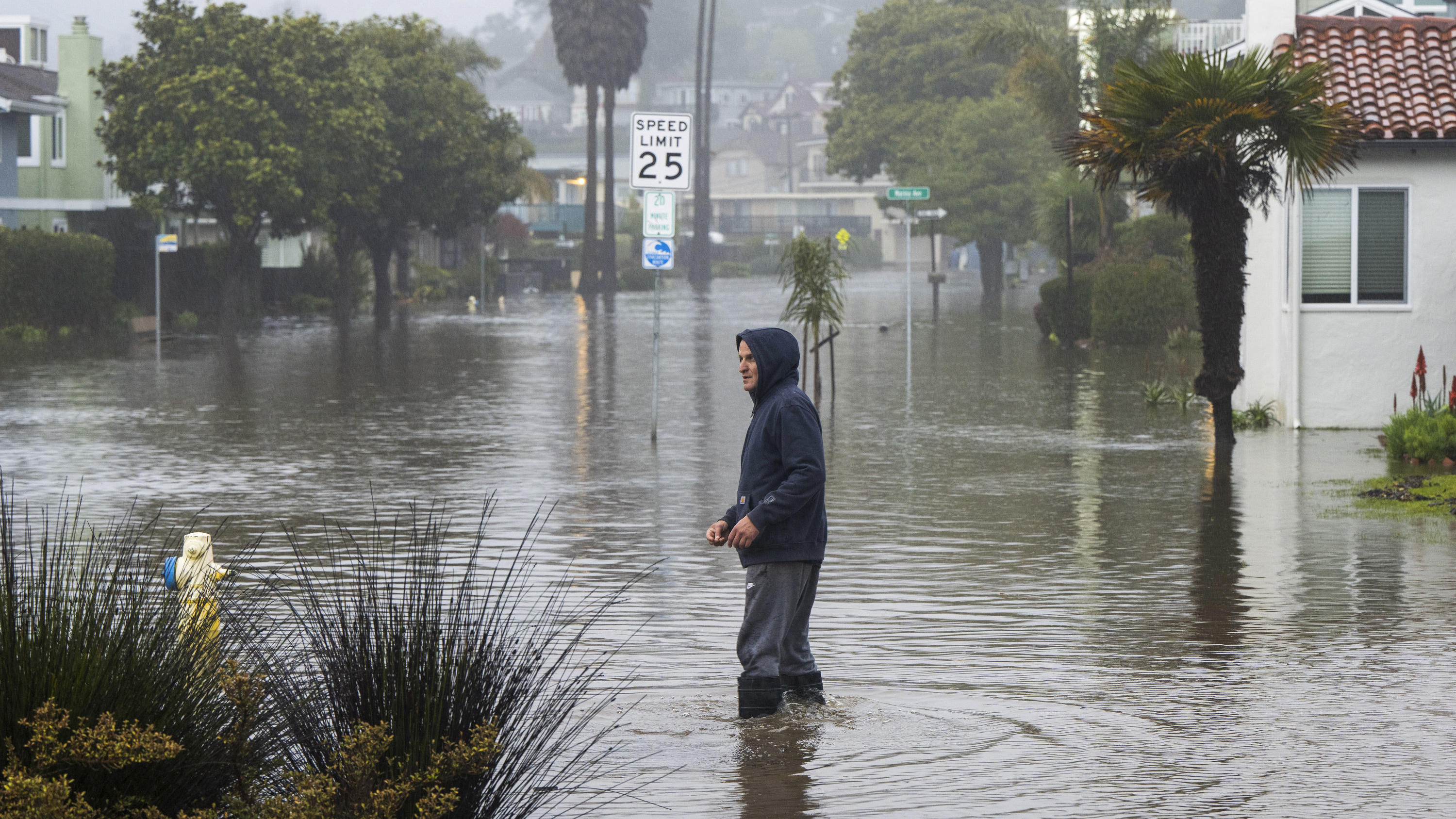 09.01.2023, USA, Aptos: Ein Mann watet durch eine überschwemmte Straße in der Nähe von Rio Del Mar. Foto: Nic Coury/FR171100 AP/dpa +++ dpa-Bildfunk +++