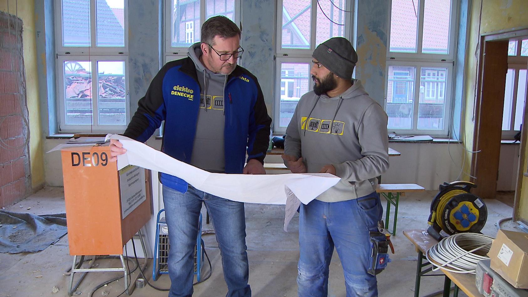 Azubi Sheraz Chaudhry und sein Meister Mathias Puchta begutachten auf der Baustelle Pläne.