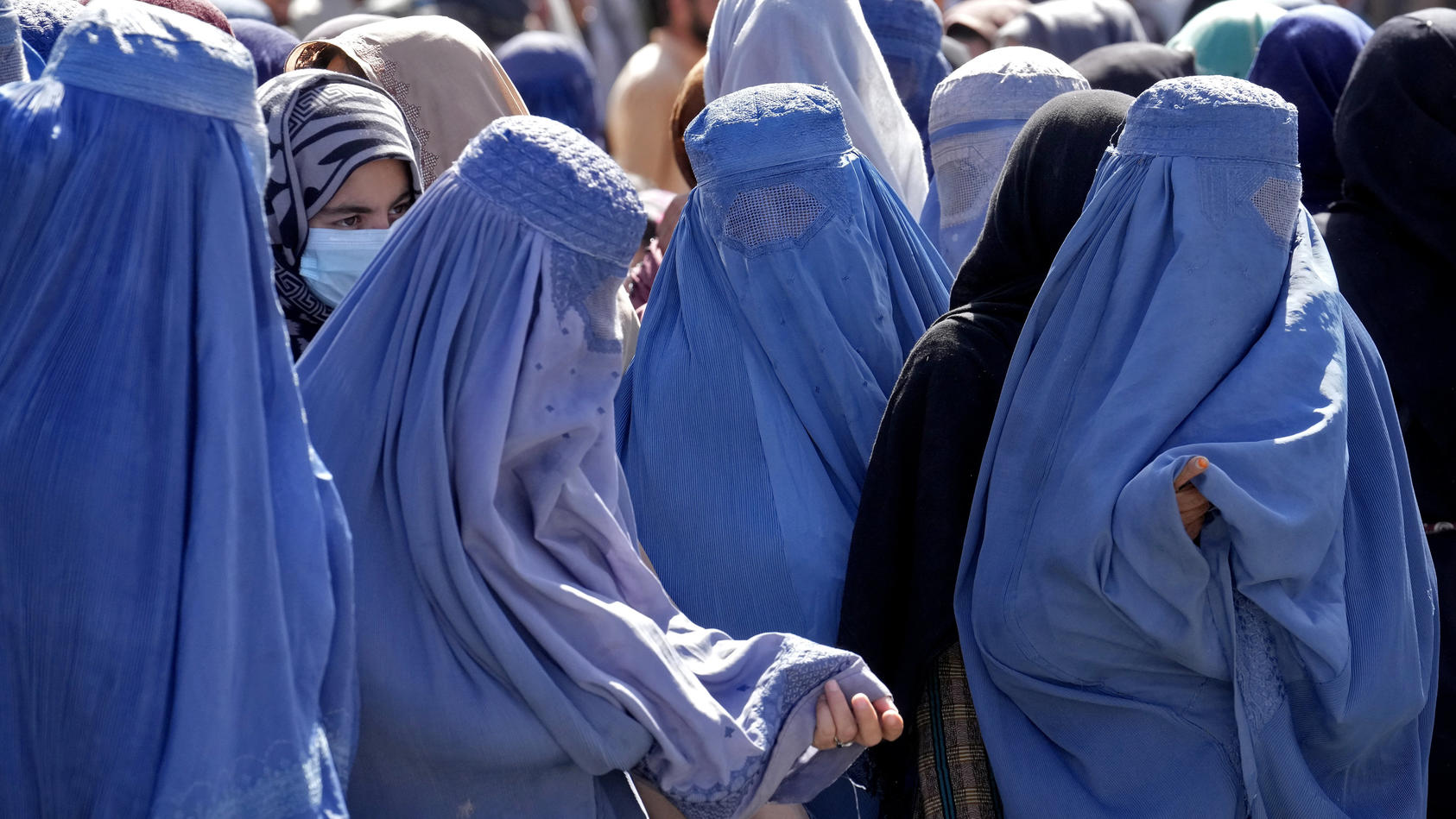 ARCHIV - 15.08.2022, Afghanistan, Kabul: Frauen in Burkas warten auf Lebensmittelrationen, die von einer humanitären Hilfsorganisation aus Saudi-Arabien verteilt werden. In Afghanistan befürchten Medienberichten zufolge Frauen weitere Einschränkungen