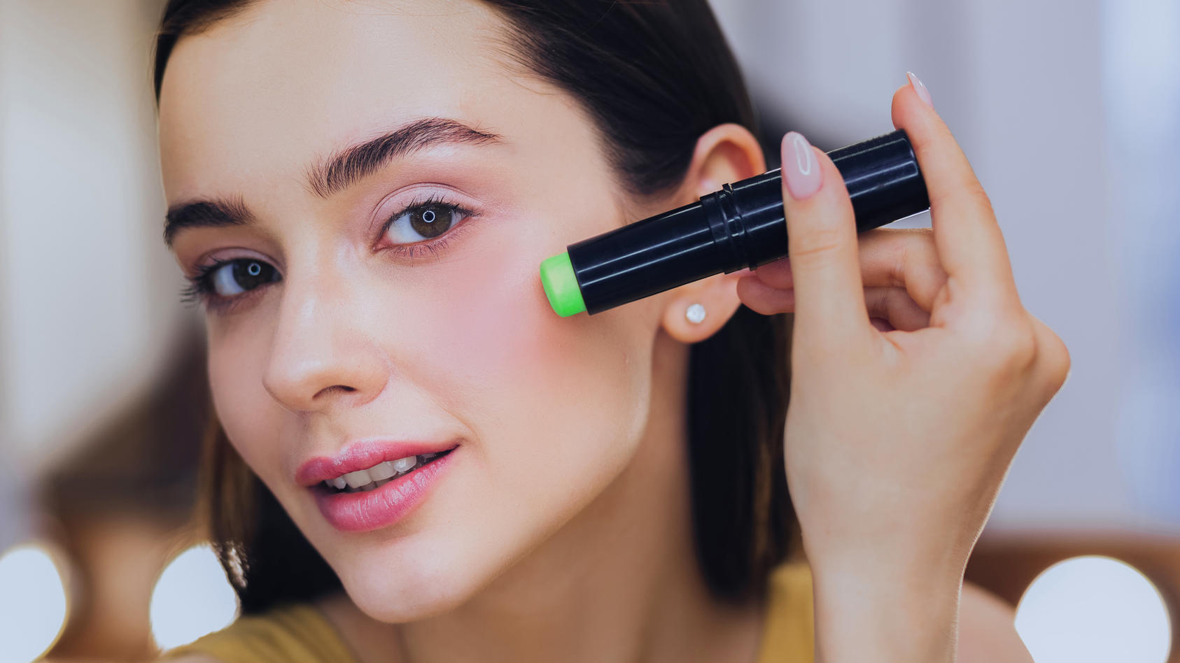 Frau trägt grünen Concealer mit Korrekturstift auf.