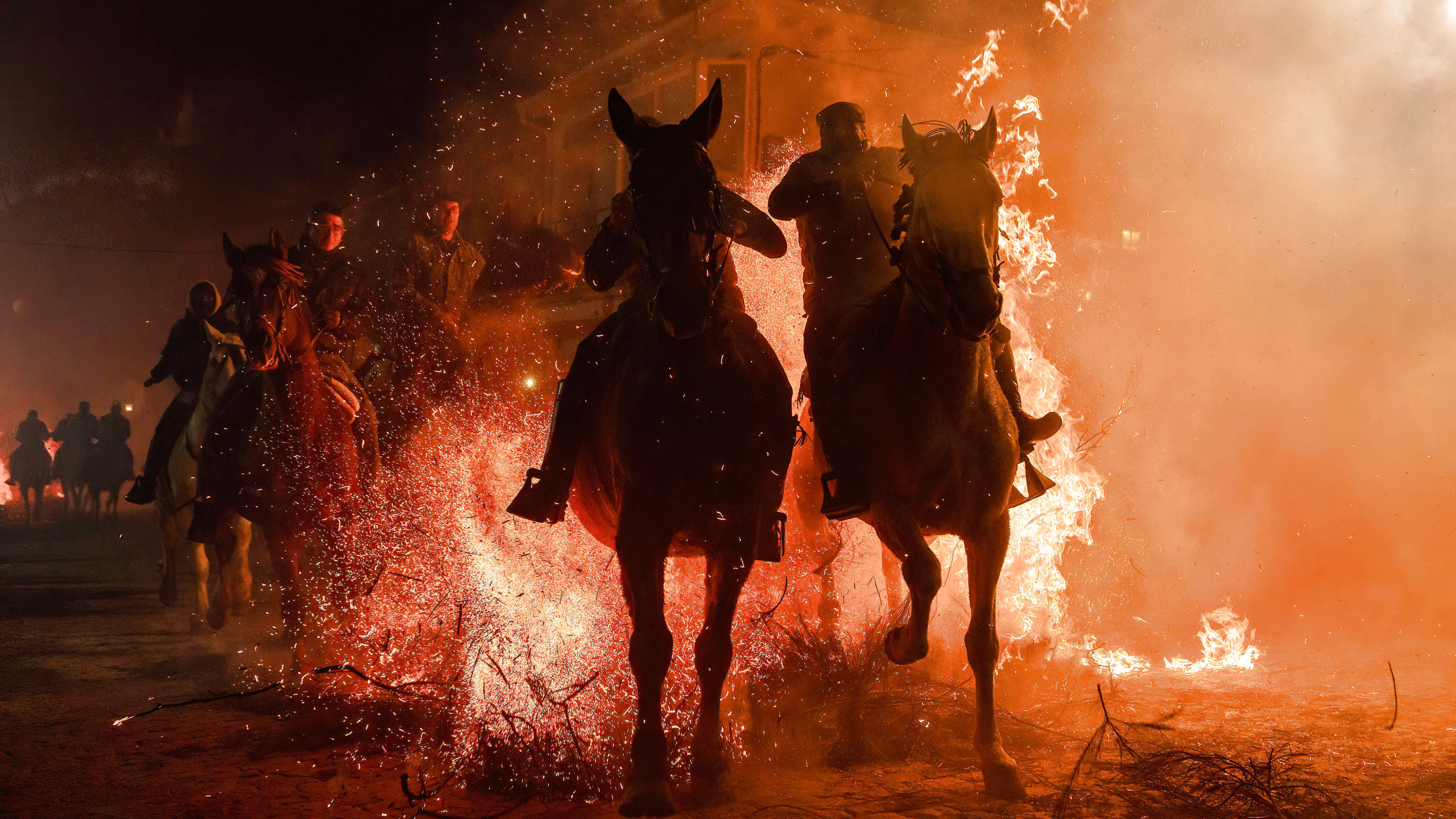Viele Reiter galoppieren mit den Pferden durch Sträucherhaufen, die in hohen Flammen stehen