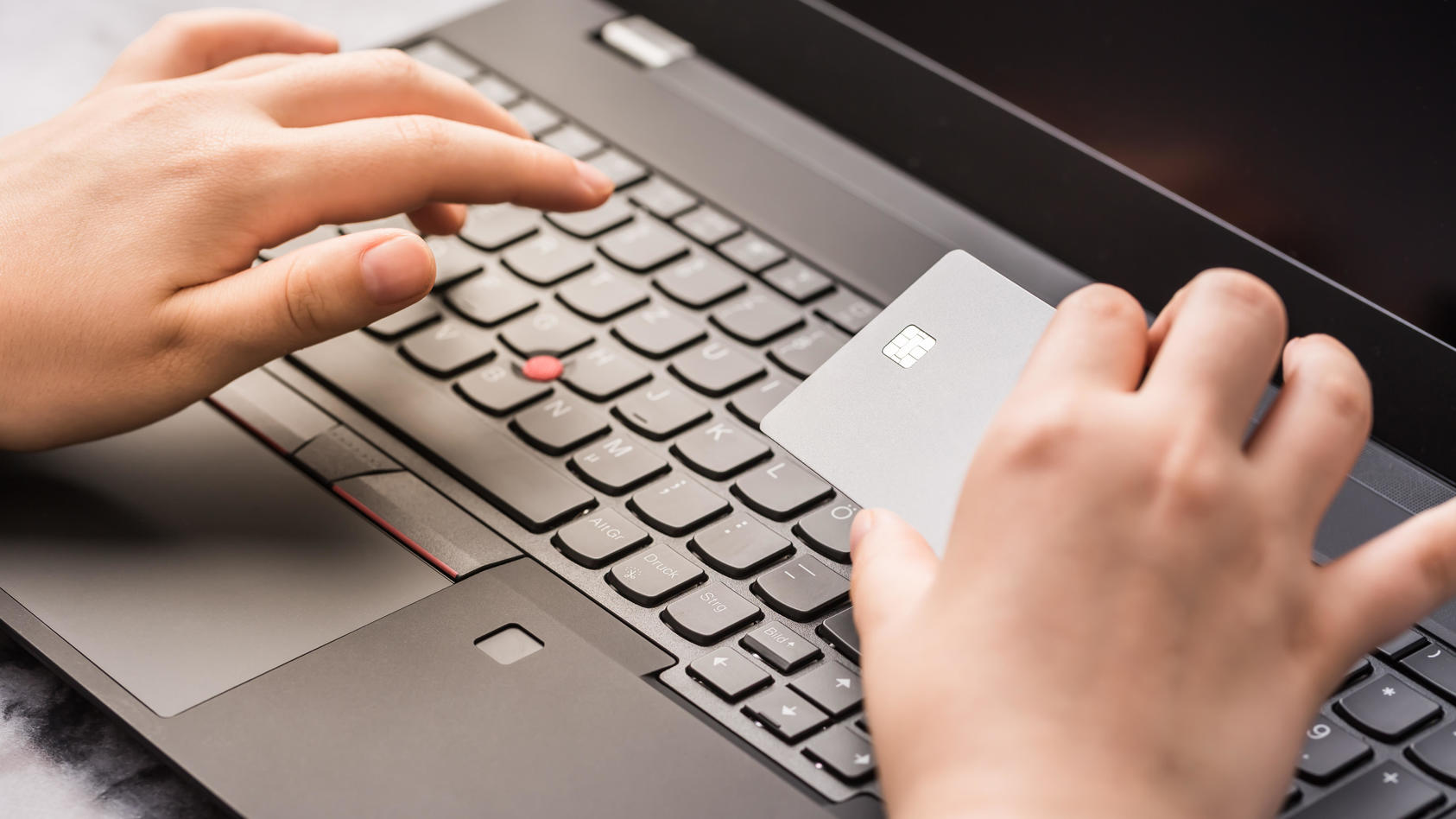 Eine Hand hält eine Kreditkarte vor einer Laptop-Tastatur