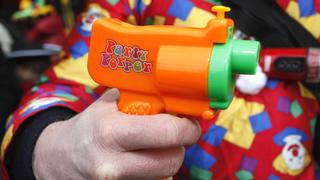 Karnevalist hält kleine, bunte Scherz-Pistole in der Hand