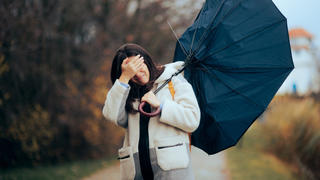 Frau kämpft im Sturm mit Regenschirm.