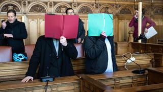 08.02.2023, Bremen: Zwei Angeklagte stehen vor Prozessbeginn im Gerichtssaal und verbergen ihre Gesichter. Drei Männern wird vorgeworfen, im April 2020 einen Mann getötet zu haben. Foto: Sina Schuldt/dpa +++ dpa-Bildfunk +++
