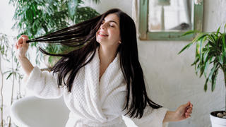 Junge Frau ist glücklich in ihrem Badezimmer und erledigt ihre Haarpflege
