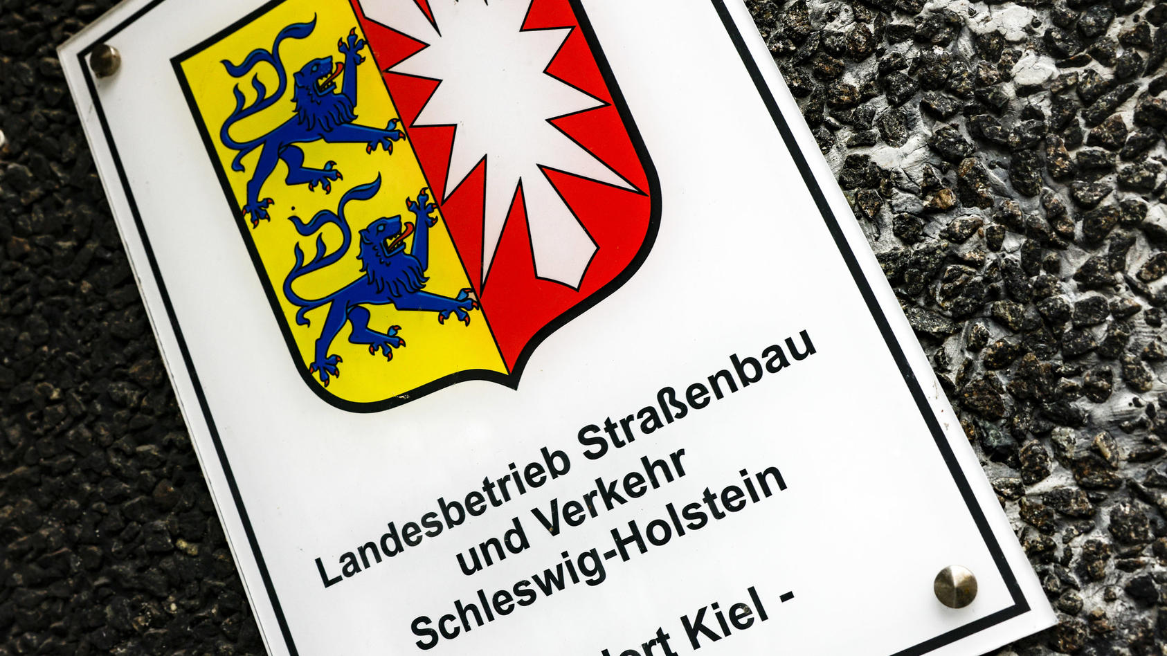 ARCHIV - 01.02.2023, Schleswig-Holstein, Kiel: Ein Hinweisschild auf den Sitz vom Landesbetrieb Straßenbau und Verkehr hängt am Eingang zur Hauptstelle. Die schleswig-holsteinische FDP kritisiert die geplante Umbenennung des Landesbetriebs.      (zu 