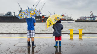 21.08.2020, Hamburg: Mit bunten Regenschirmen schützten sich zwei Jungen im Hafen Hamburg vor dem Regen. Nach vielen trockenen, sonnigen Tagen regnet es wieder in der Hansestadt. Foto: Ulrich Perrey/dpa - ACHTUNG: Nur zur redaktionellen Verwendung im Zusammenhang mit der aktuellen Berichterstattung und nur mit vollständiger Nennung des vorstehenden Credits +++ dpa-Bildfunk +++