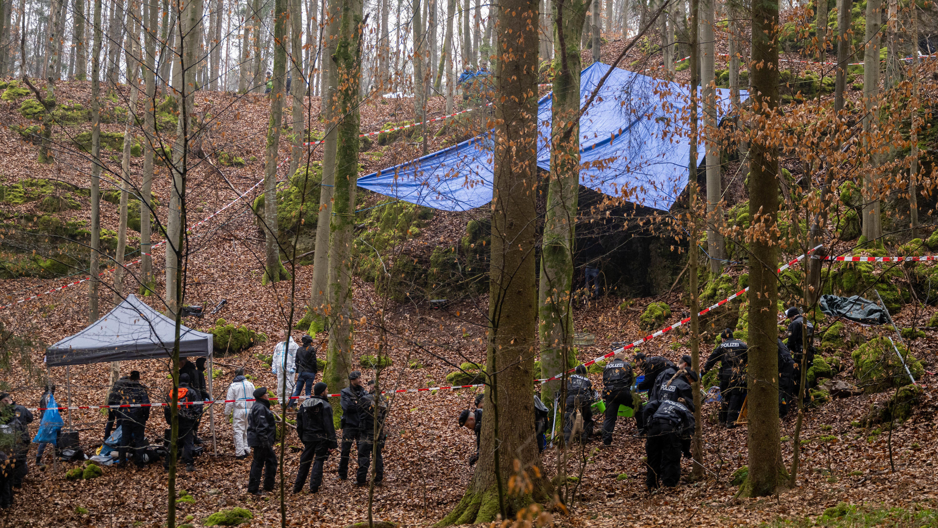 ARCHIV - 30.03.2022, Bayern, Größdorf: Polizisten suchen ein Gebiet im Wald ab, an dem zuvor menschliche Knochen in einer Felsspalte gefunden worden sind. Die Ermittlungen ergaben einen Zusammenhang mit dem Fall der seit 1995 vermissten und wohl ermo