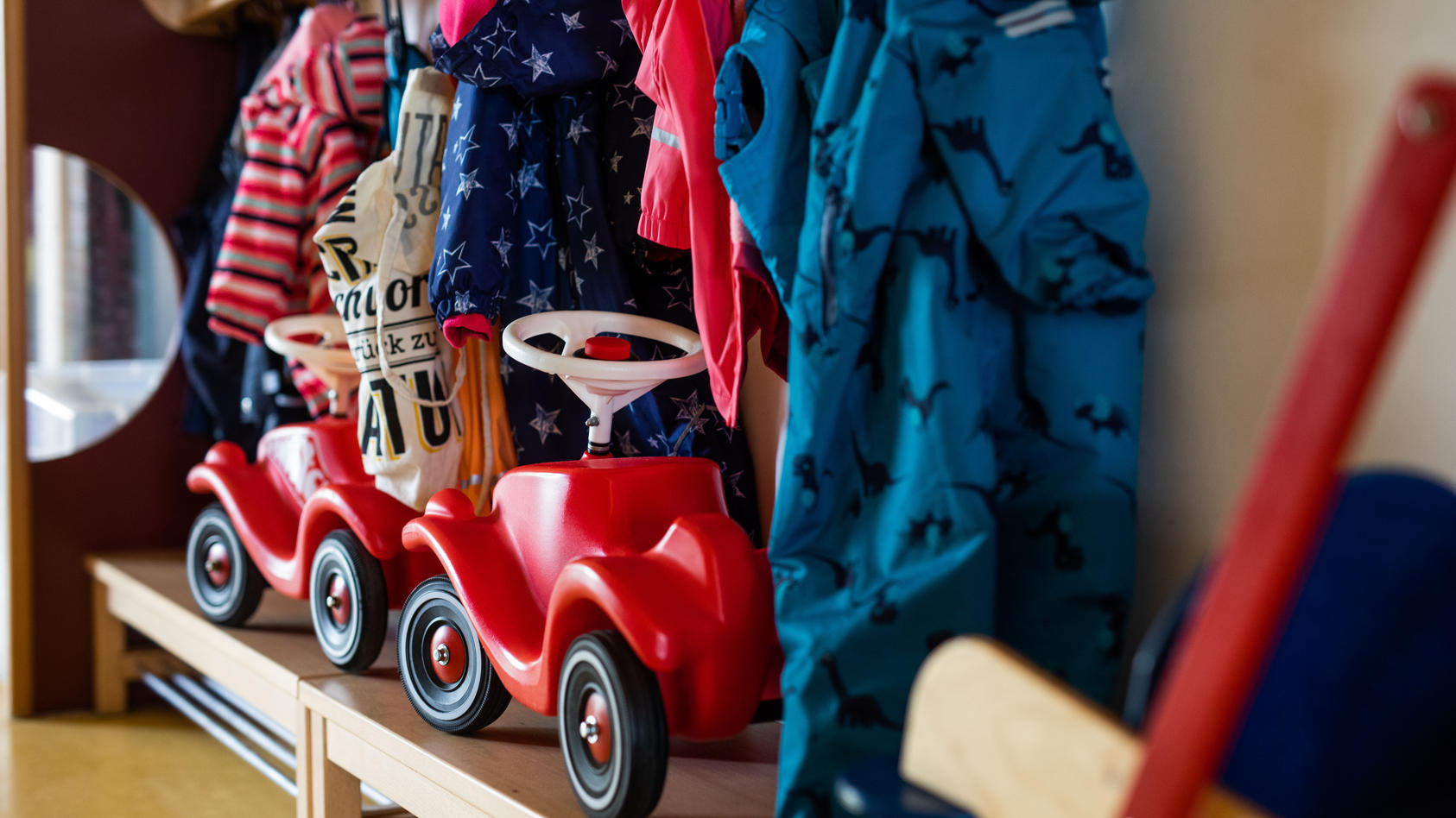 Bobbycars stehen in einer Garderobe auf Bänken unter Jacken von Kindern einer Kindertagesstätte.