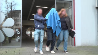 Zwei Polizisten führen den Tatverdächtigen (Mitte) aus dem Amtsgericht Osnabrück. Der 20-Jährige trägt noch Hausschuhe. Sein Gesicht verhüllt er mit einer blauen Decke.