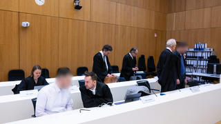 06.03.2023, Bayern, München: Die zwei wegen Mordes angeklagten Männer (2.v.l. und r) stehen vor Beginn der Verhandlung im Hochsicherheitsgerichtssaal vom Landgericht München II neben ihren Rechtsanwälten Sarah Stolle (l), Alexander Stevens (3.v.l.), Alexander Betz (4.v.l.), Patrick Ottmann (5.v.l.) und Gerhard Bink (2.v.r.). Im Prozess geht es um einen mutmaßlichen Dreifachmord in Starnberg im Januar 2020. Die beiden angeklagten Männer müssen sich wegen Mordes, besonders schweren Raubes und Verstoßes gegen das Kriegswaffenkontrollgesetz verantworten. Foto: Sven Hoppe/dpa - ACHTUNG: Person(en) wurde(n) aus rechtlichen Gründen gepixelt +++ dpa-Bildfunk +++