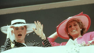 Sarah Ferguson und Lady Diana in 1987. Beide Frauen tragen Hüte. Sarah Ferguson schaut errschreckt und überrascht, Lady Diana grinst.