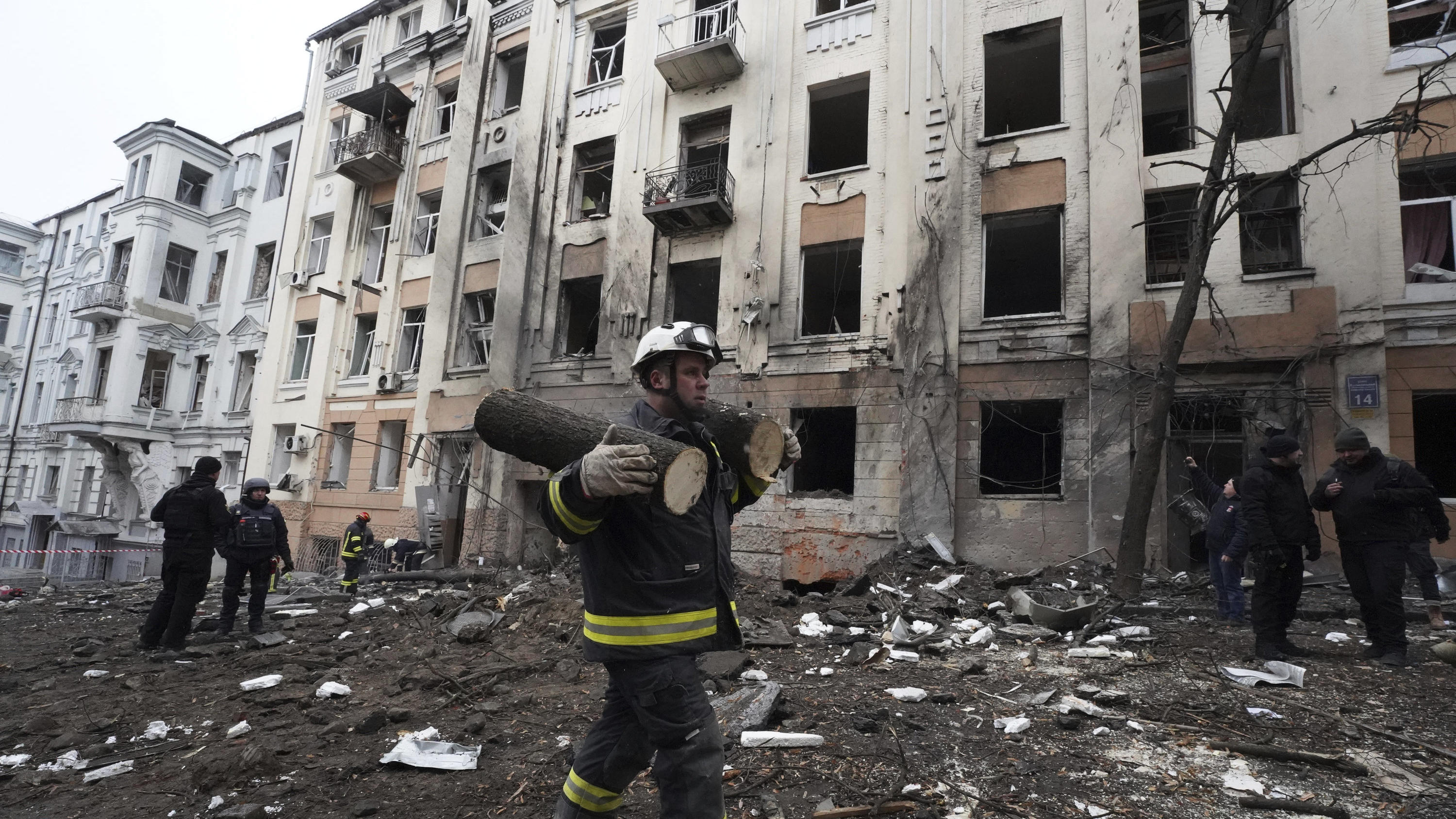 05.02.2023, Ukraine, Charkiw: Eine Rettungskraft trägt Teile eines abgesägten Baumes vor einem Wohnhaus, das von einer russischen Rakete getroffen wurde. Foto: Andrii Marienko/AP/dpa +++ dpa-Bildfunk +++