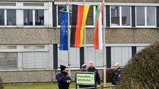 13.03.2023, Nordrhein-Westfalen, Freudenberg: Mitarbeiter des Ordnungsamtes stehen vor dem Schulzentrum des ermordeten Mädchens. Die Schule hat geöffnet, die Fahnen sind auf Halbmast geflaggt und die Schüler werden von Therapeuten begleitet. In einem Waldstück wurde gestern die Leiche eines 12jährigen Mädchens gefunden. Das Mädchen wurde am Samstag vermisst und die Polizei startete eine groß angelegte Suchaktion, bei der die Leiche am Sonntag entdeckt wurde. Foto: Roberto Pfeil/dpa - ACHTUNG: Person(en) wurde(n) aus rechtlichen Gründen gepixelt +++ dpa-Bildfunk +++