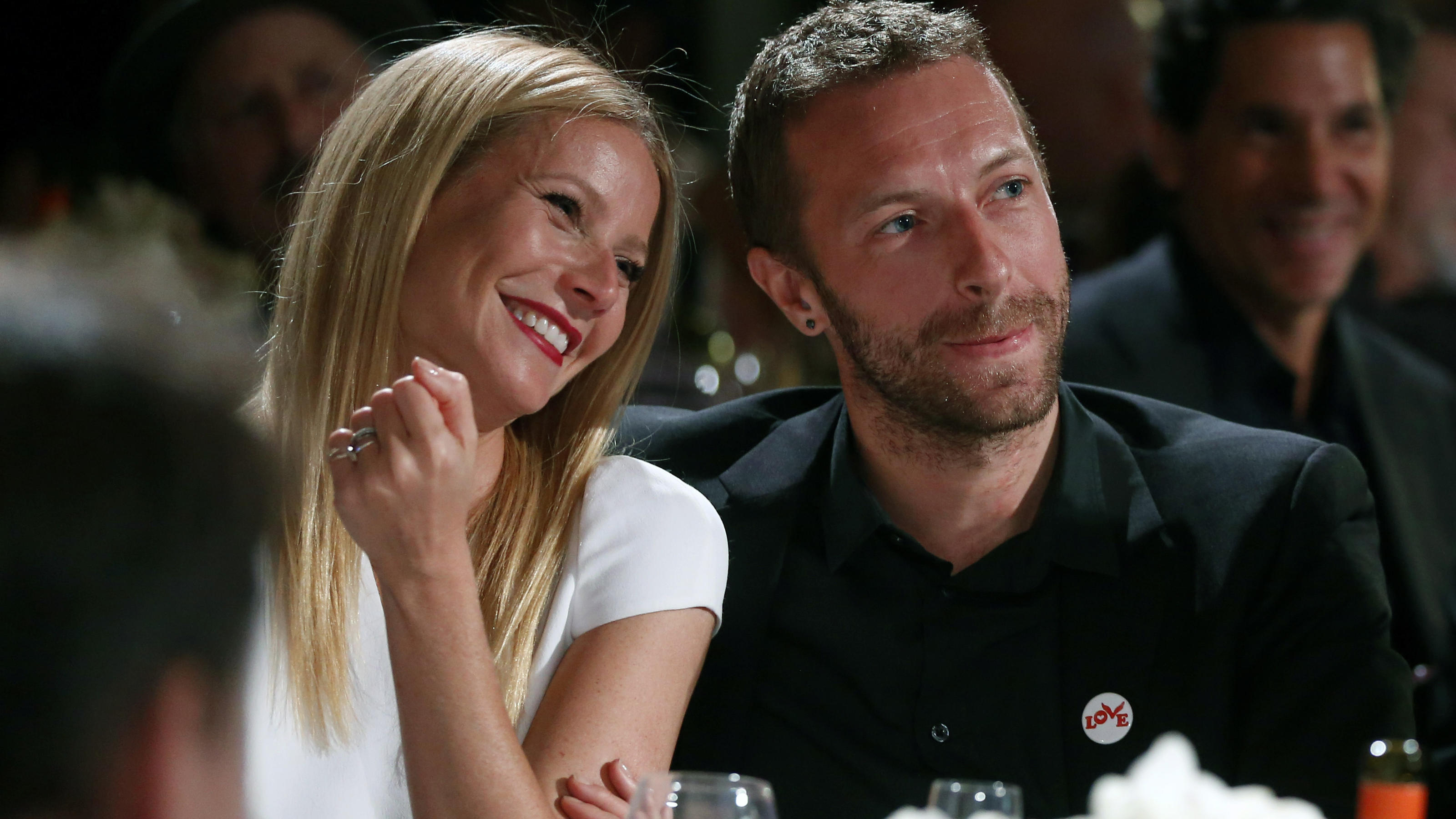 Gwyneth Paltrow und Chris Martin sitzen bei einer Gala nebeneinander und lachen.