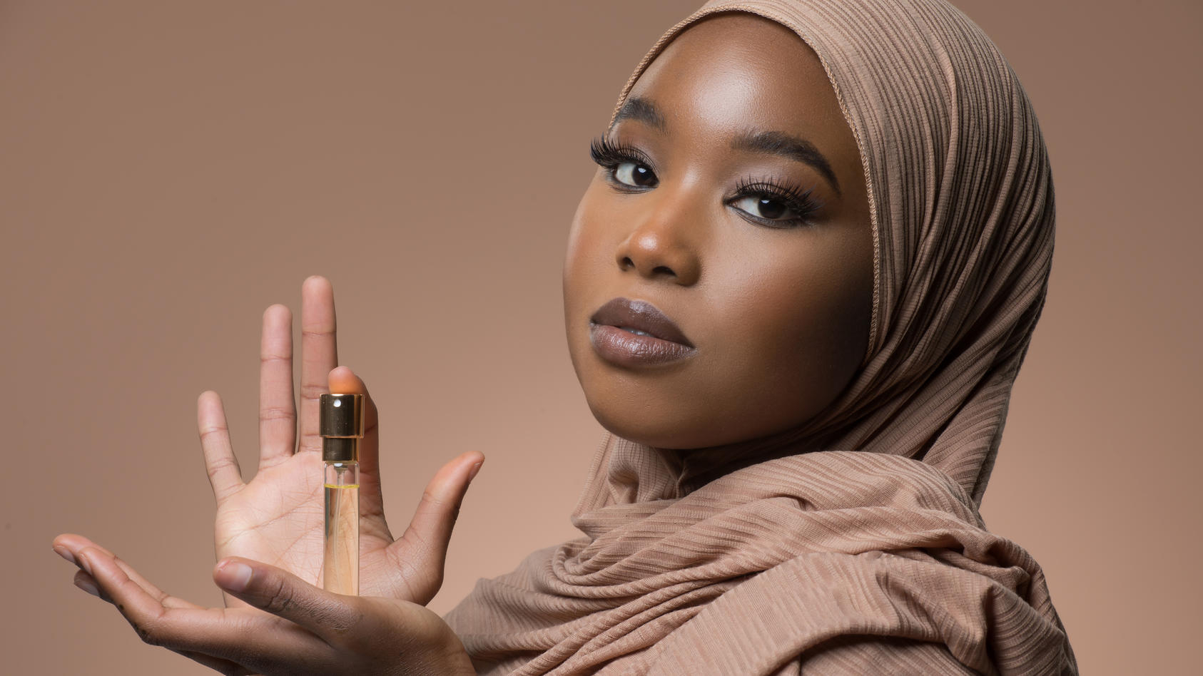 Frau mit Hijab, die eine Flasche Parfum in der Hand hält.