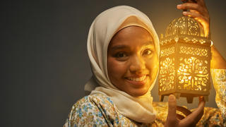 Frau mit Hijab hält eine Laterne in der Hand.