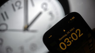 PRODUKTION - 21.03.2023, Hessen, Gießen: Ein Smartphone zeigt die Uhrzeit «03:03» an, während auf einer analogen Uhr noch 02:03 Uhr ist. Am 26. März werden die Uhren um 02:00 Uhr auf 03:00 Uhr vorgestellt und die Sommerzeit beginnt. (zu dpa: Adieu Analoguhr? Wie Zeigeruhren weniger werden) Foto: Sebastian Christoph Gollnow/dpa +++ dpa-Bildfunk +++