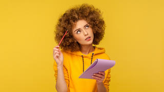 Frau mit Block und Stift in der Hand grübelt